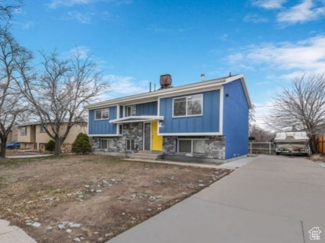 Bi-level home with stone siding, board and batten siding, fence, and driveway