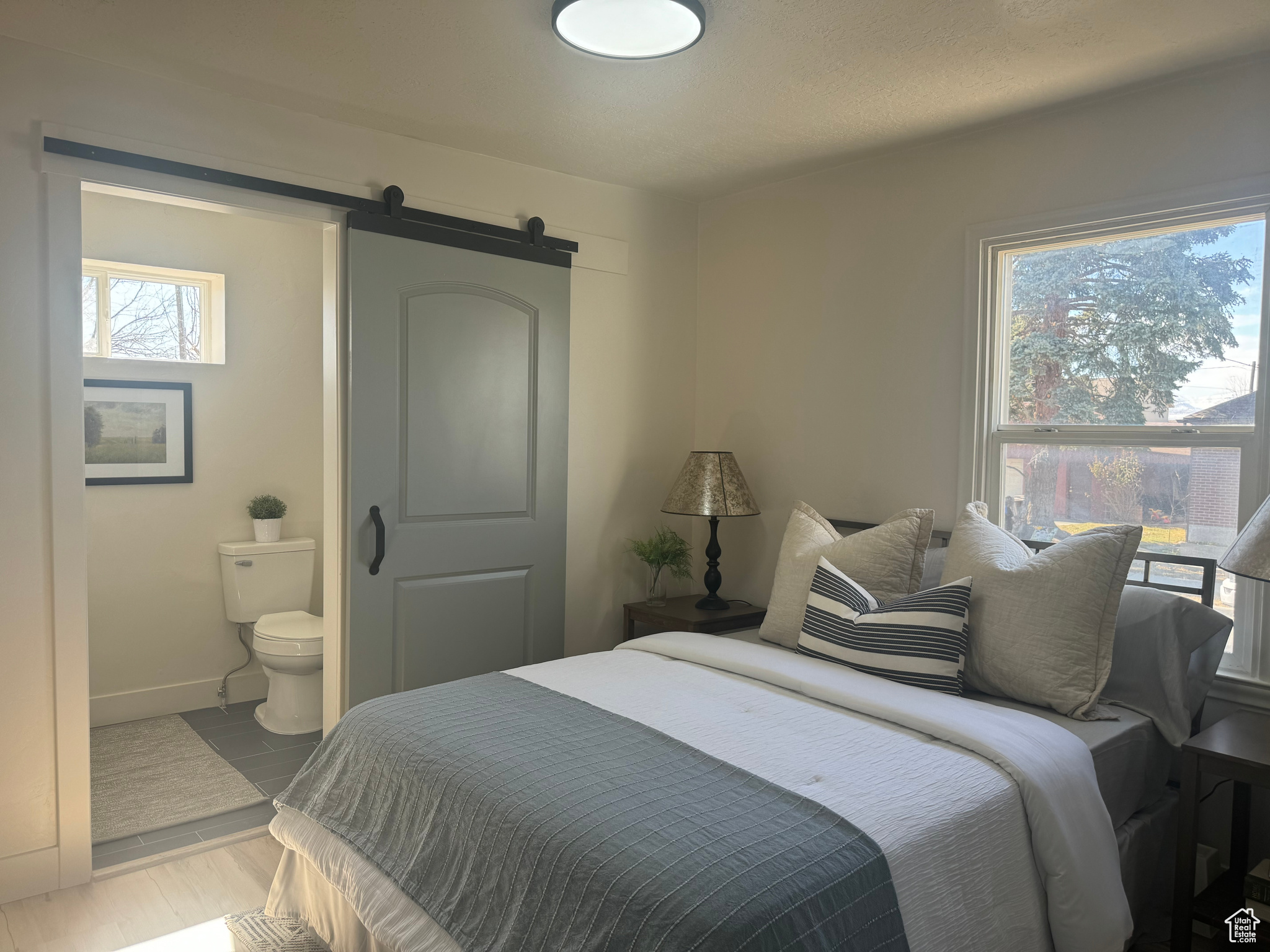 Bedroom featuring light wood finished floors, a barn door, connected bathroom, and baseboards