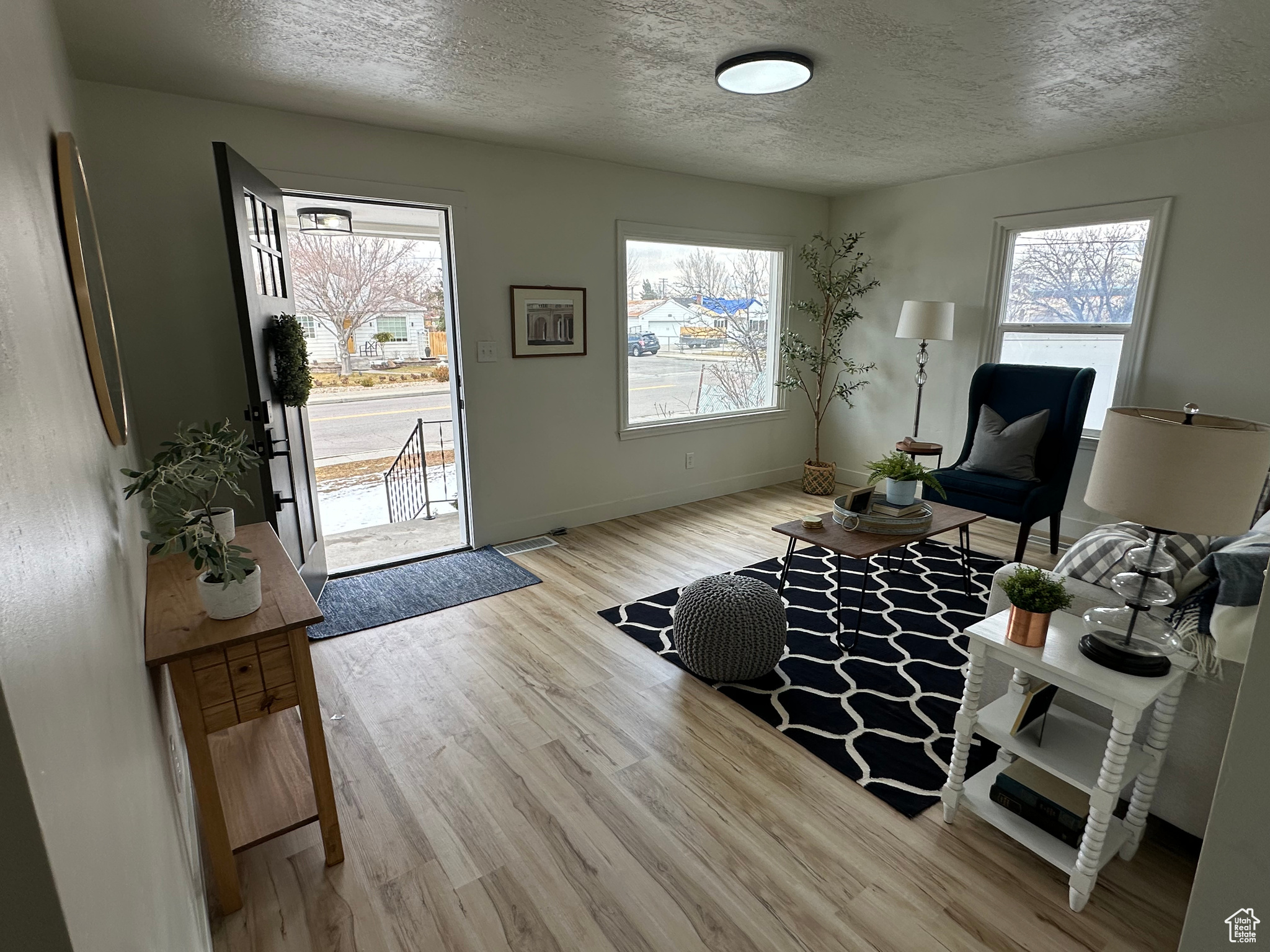 Living area featuring light wood-type flooring, a healthy amount of sunlight, a textured ceiling, and baseboards