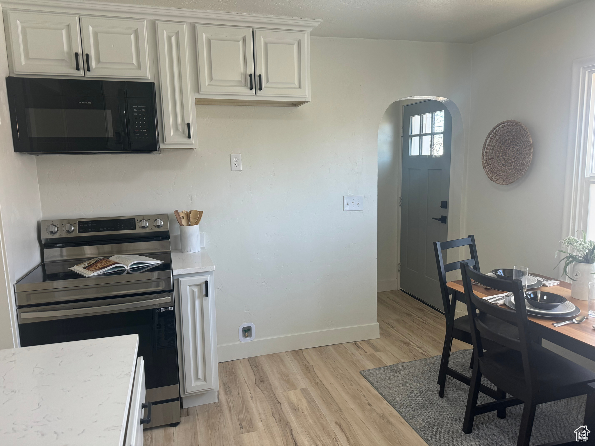 Kitchen featuring arched walkways, white cabinets, light countertops, stainless steel range with electric stovetop, and black microwave