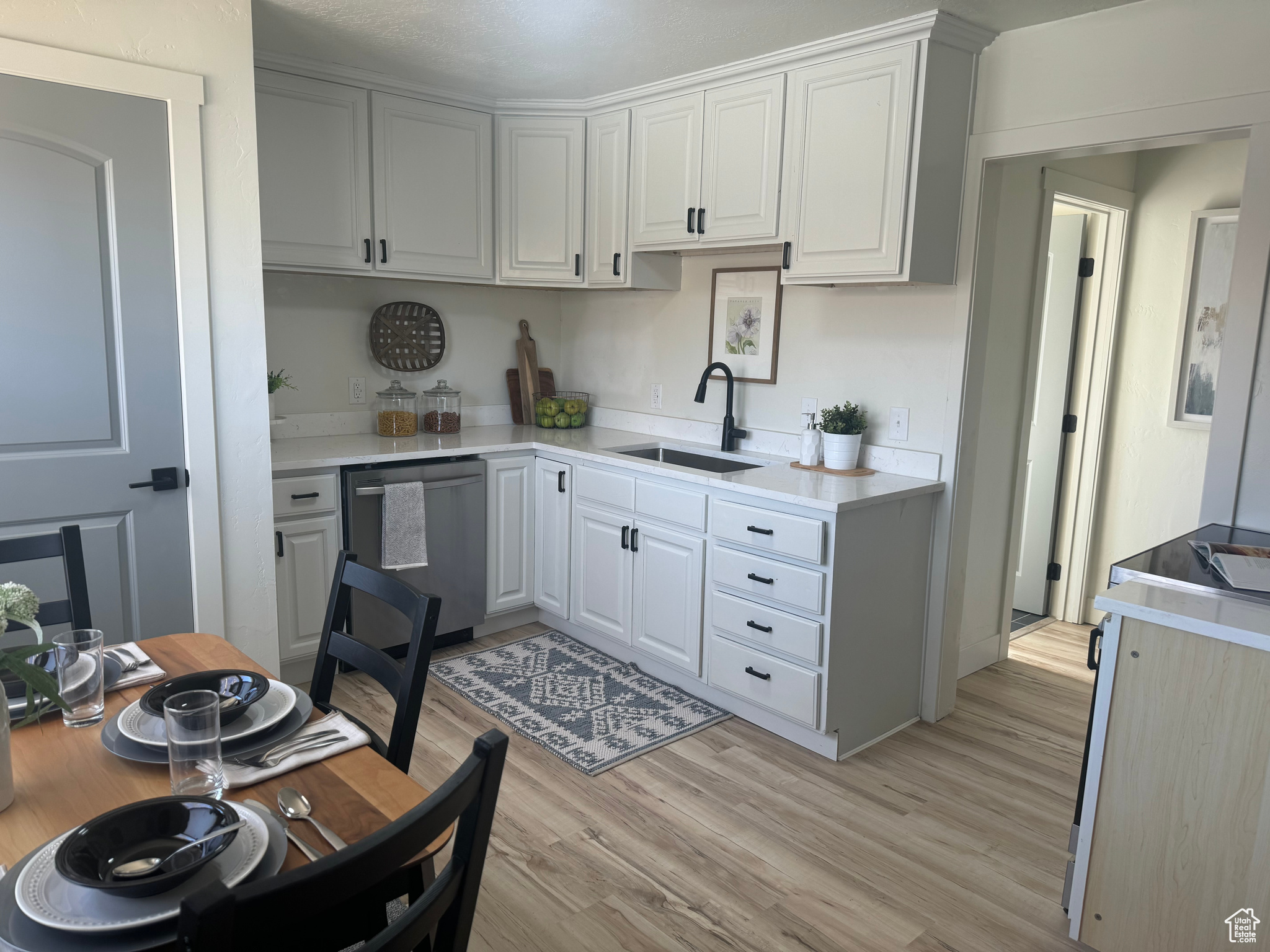 Kitchen with white cabinets, light countertops, a sink, and stainless steel dishwasher
