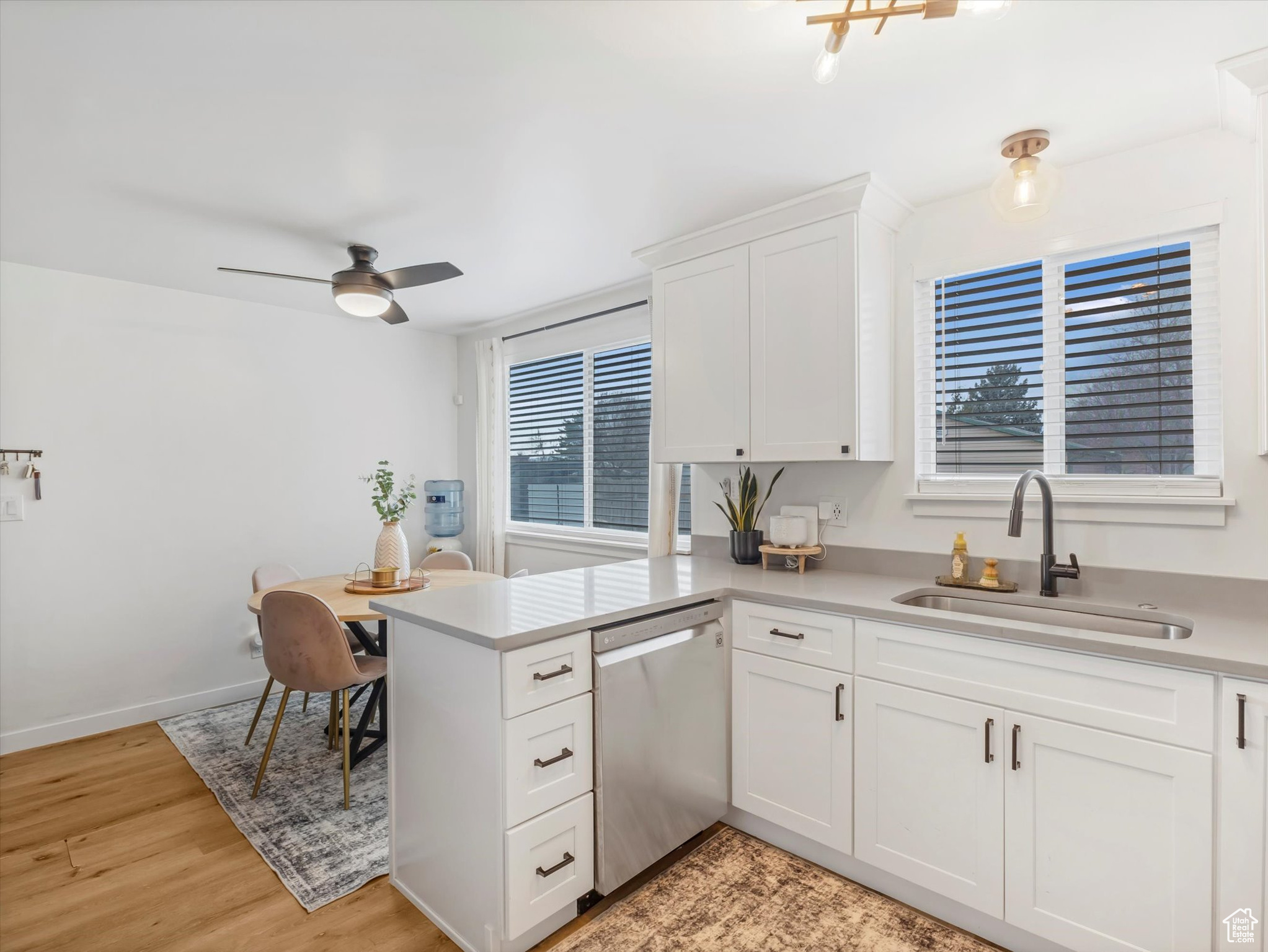 Kitchen featuring a sink, stainless steel dishwasher, a peninsula, white cabinets, and light countertops