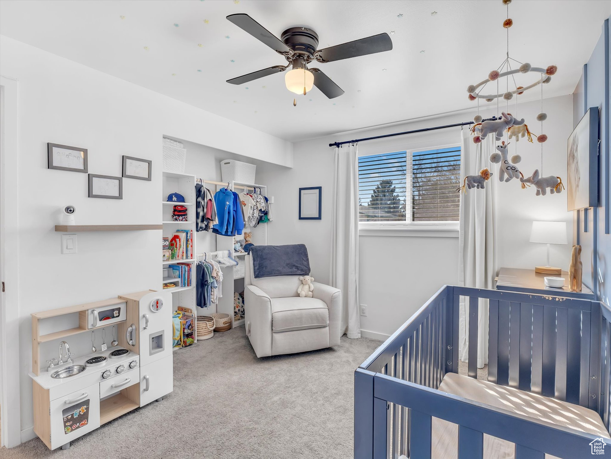 Carpeted bedroom with a crib, ceiling fan, and a closet