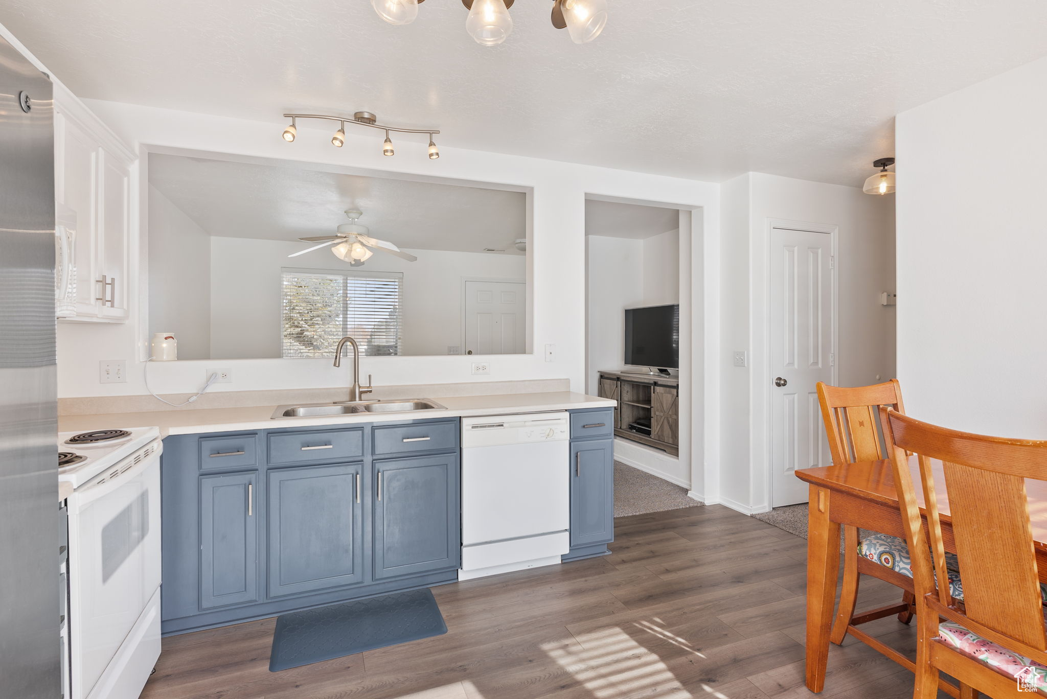 Kitchen with light countertops, dark wood-type flooring, a sink, blue cabinets, and white appliances