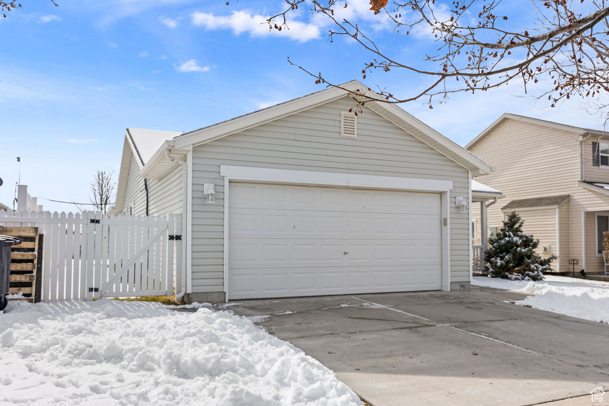 Snow covered garage featuring a gate, a detached garage, and fence