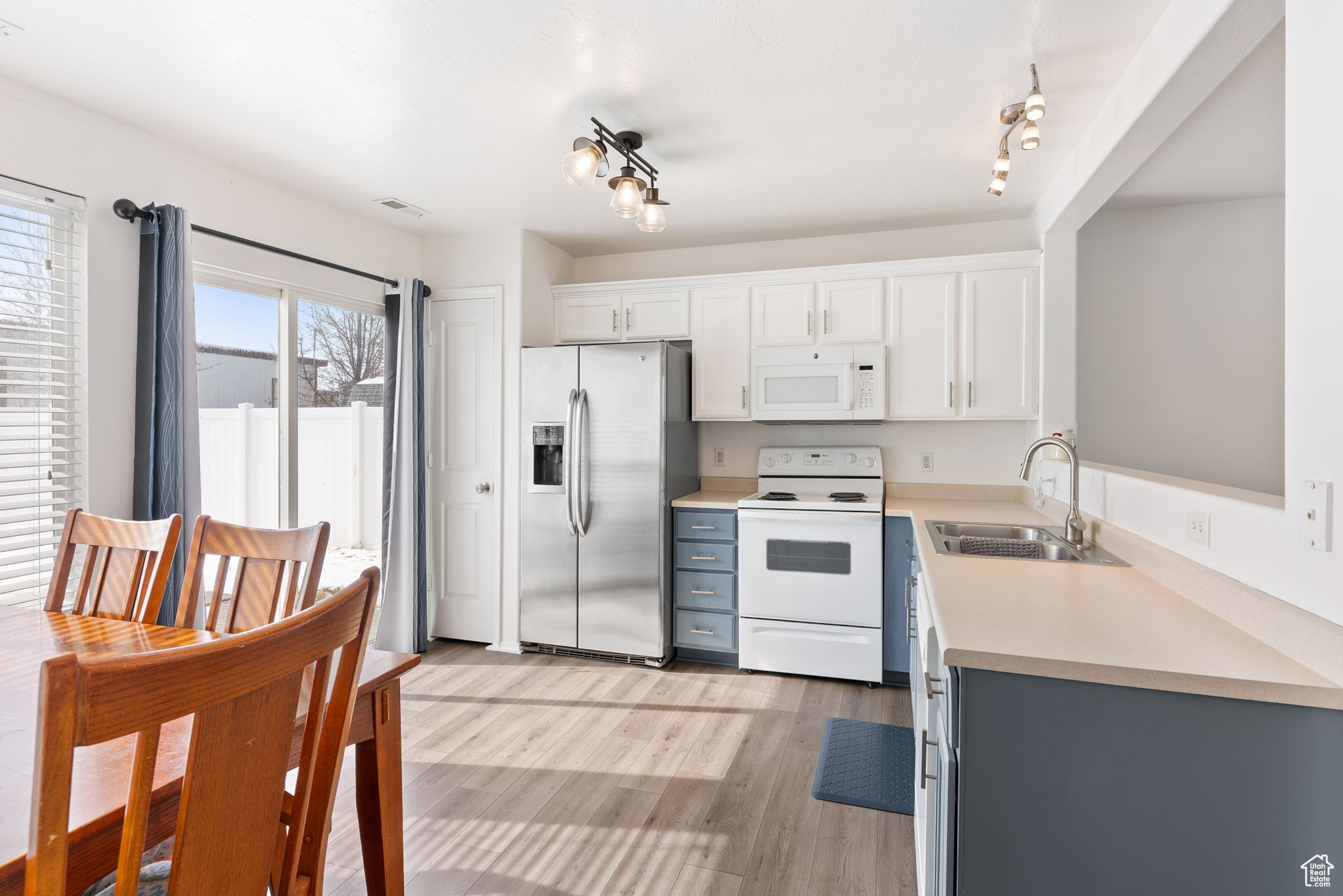 Kitchen featuring white appliances, a sink, light wood-style floors, white cabinets, and light countertops