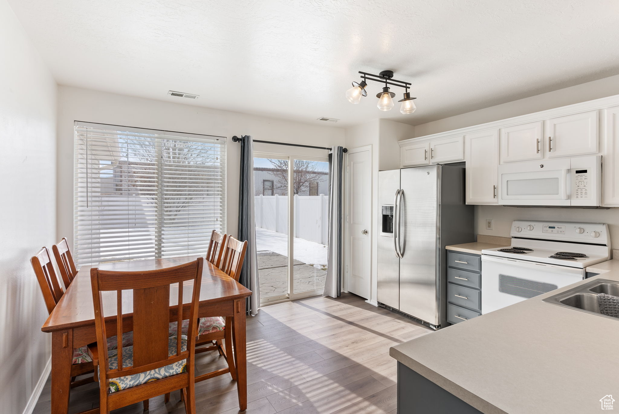 Kitchen with light countertops, visible vents, light wood-style flooring, white cabinetry, and white appliances