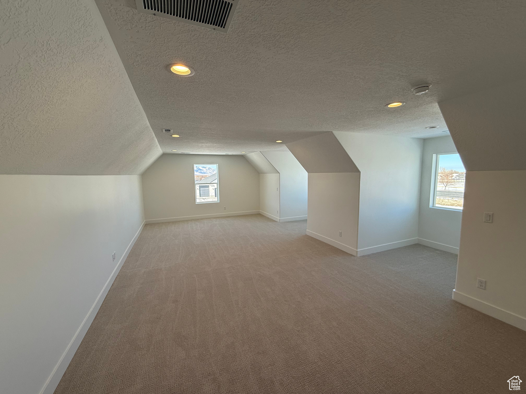 Bonus room featuring visible vents, light carpet, vaulted ceiling, a textured ceiling, and baseboards