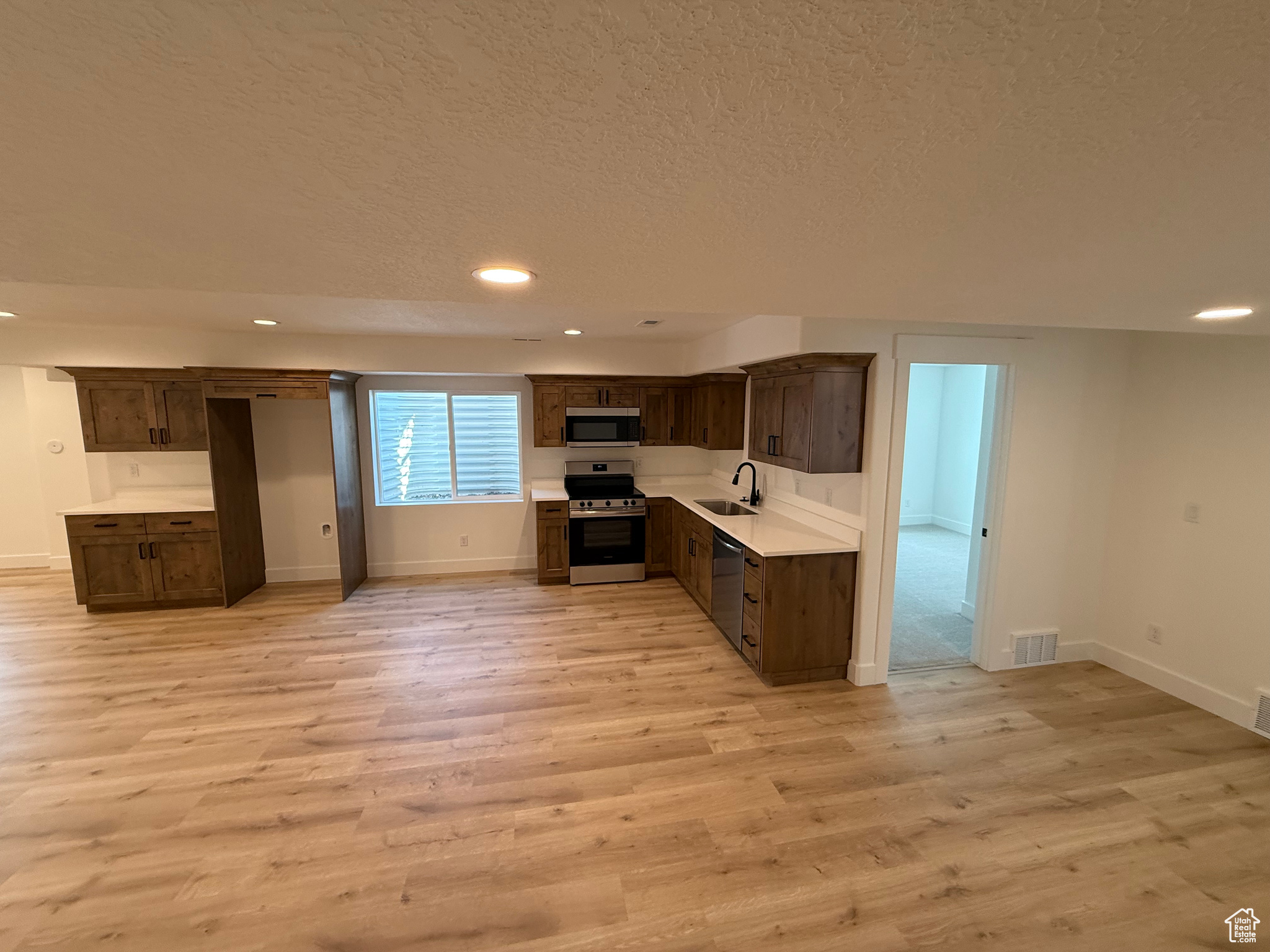 Kitchen featuring light wood finished floors, a sink, a textured ceiling, stainless steel appliances, and light countertops