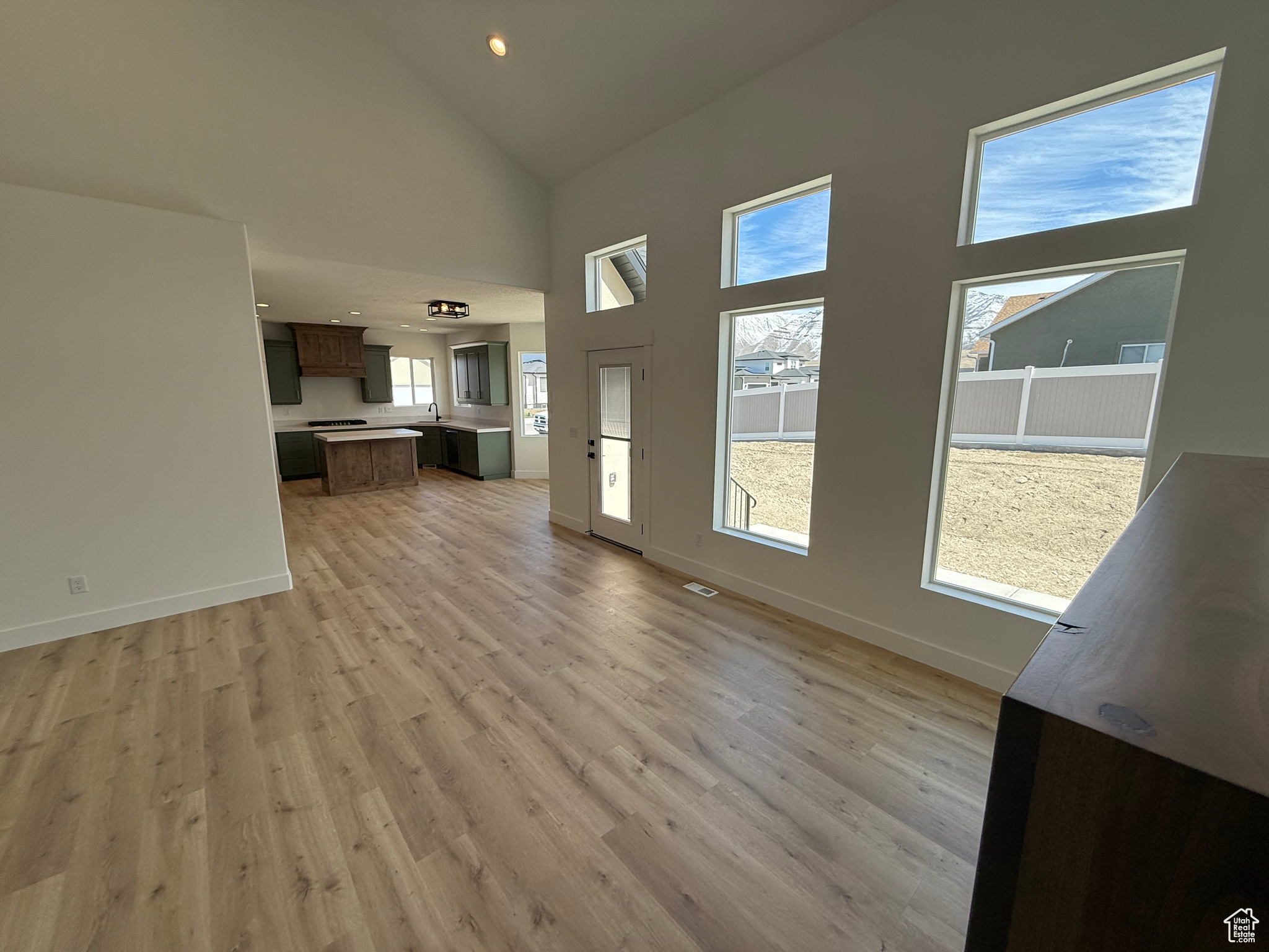 Unfurnished living room with recessed lighting, baseboards, light wood finished floors, and high vaulted ceiling