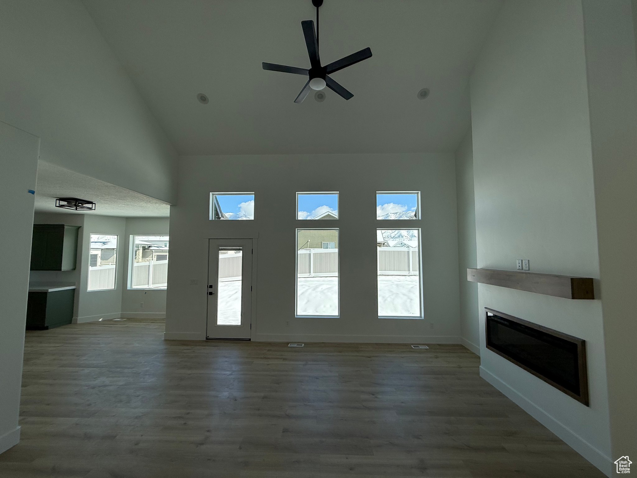 Unfurnished living room with baseboards, high vaulted ceiling, dark wood-type flooring, and a glass covered fireplace