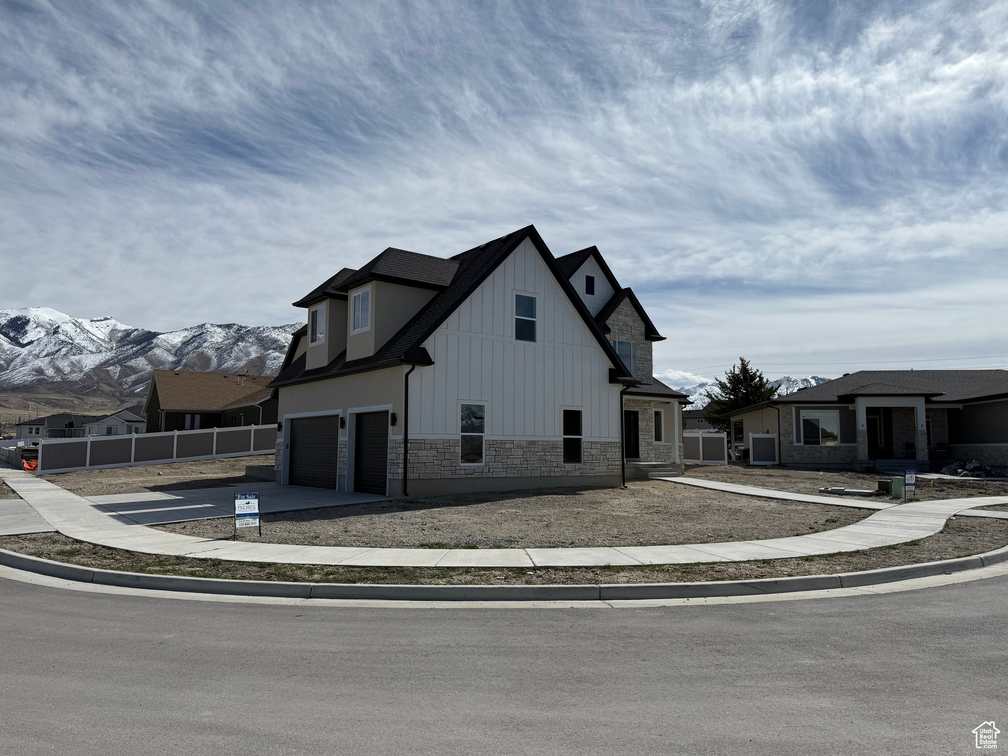 View of home's exterior with fence, driveway, a garage, stone siding, and board and batten siding