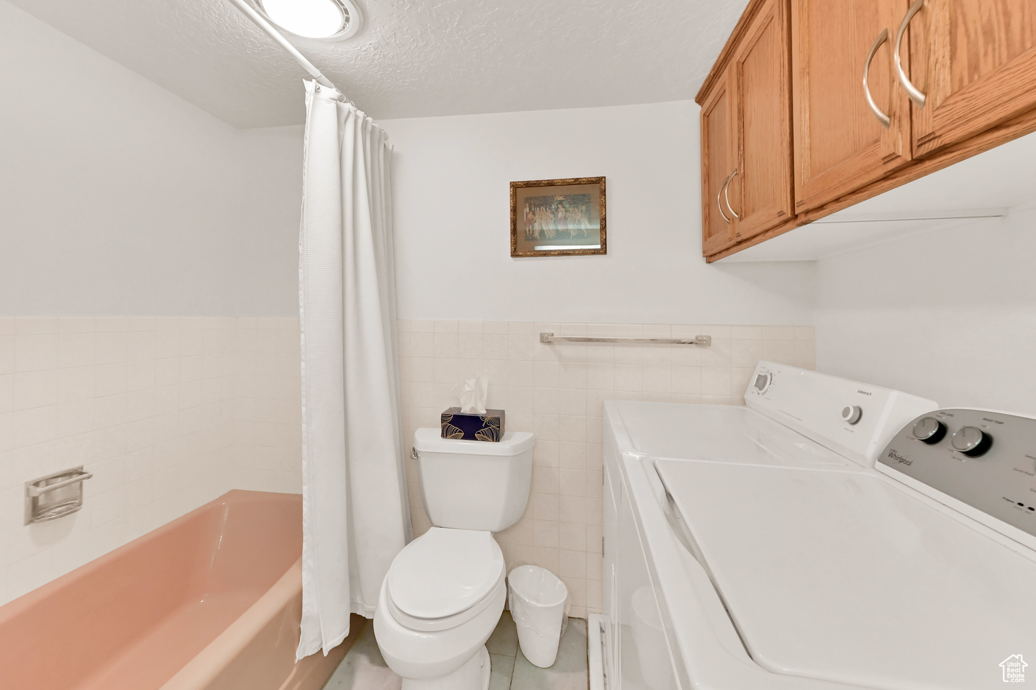 Interior space featuring laundry area, a wainscoted wall, washing machine and clothes dryer, a textured ceiling, and tile walls