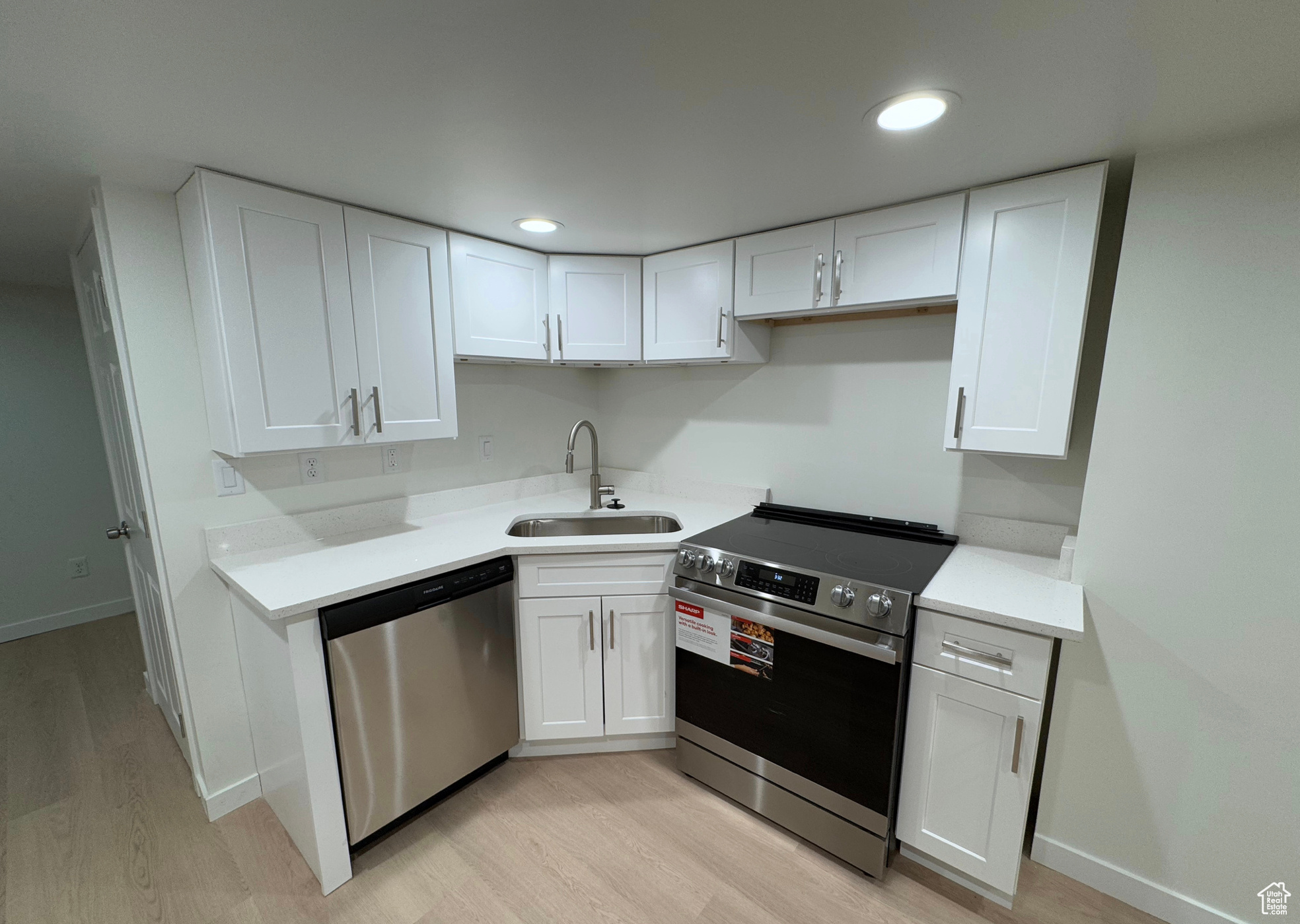 Kitchen with stainless steel appliances, a sink, white cabinets, light countertops, and light wood finished floors