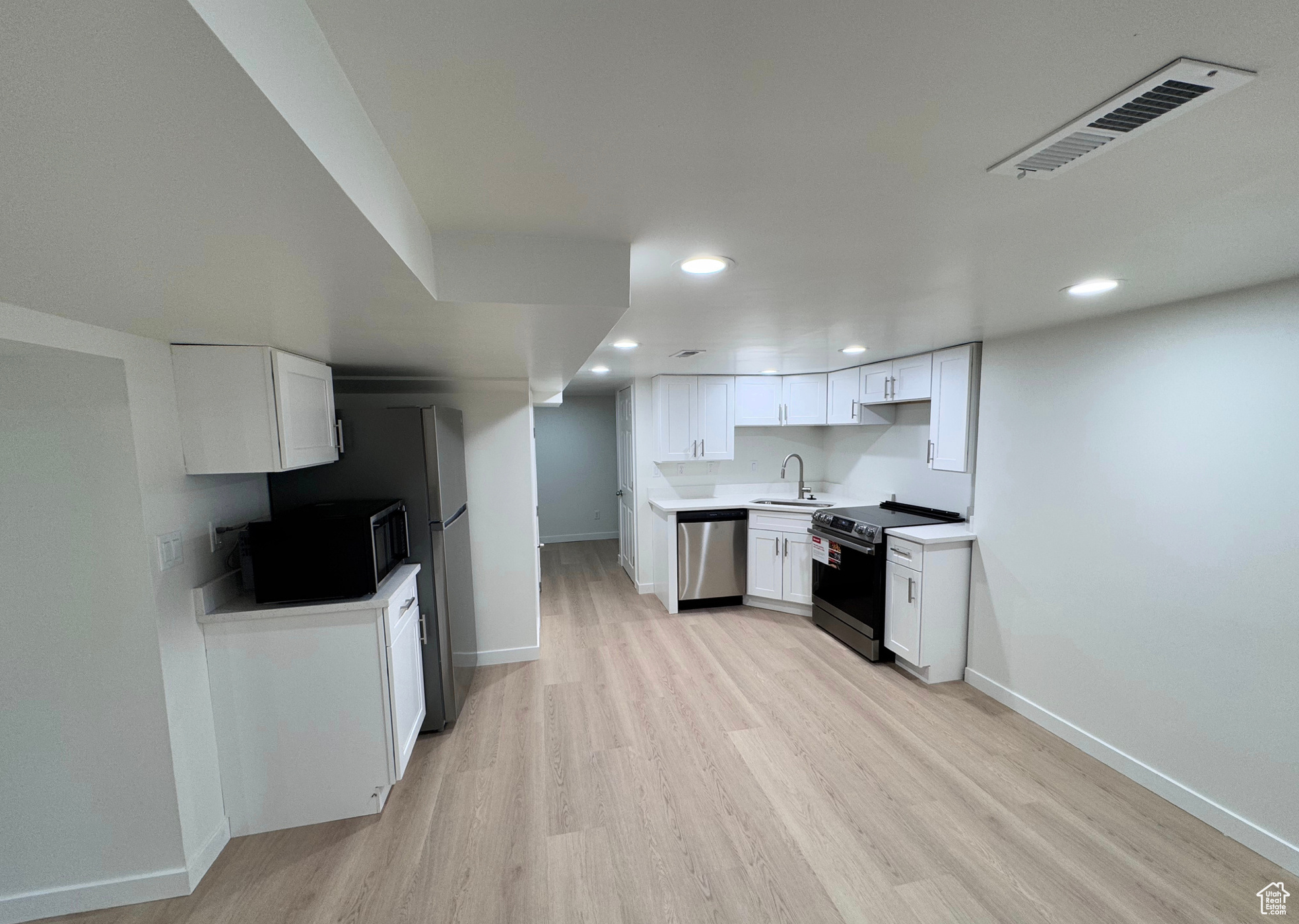 Kitchen featuring stainless steel appliances, white cabinets, light countertops, and visible vents