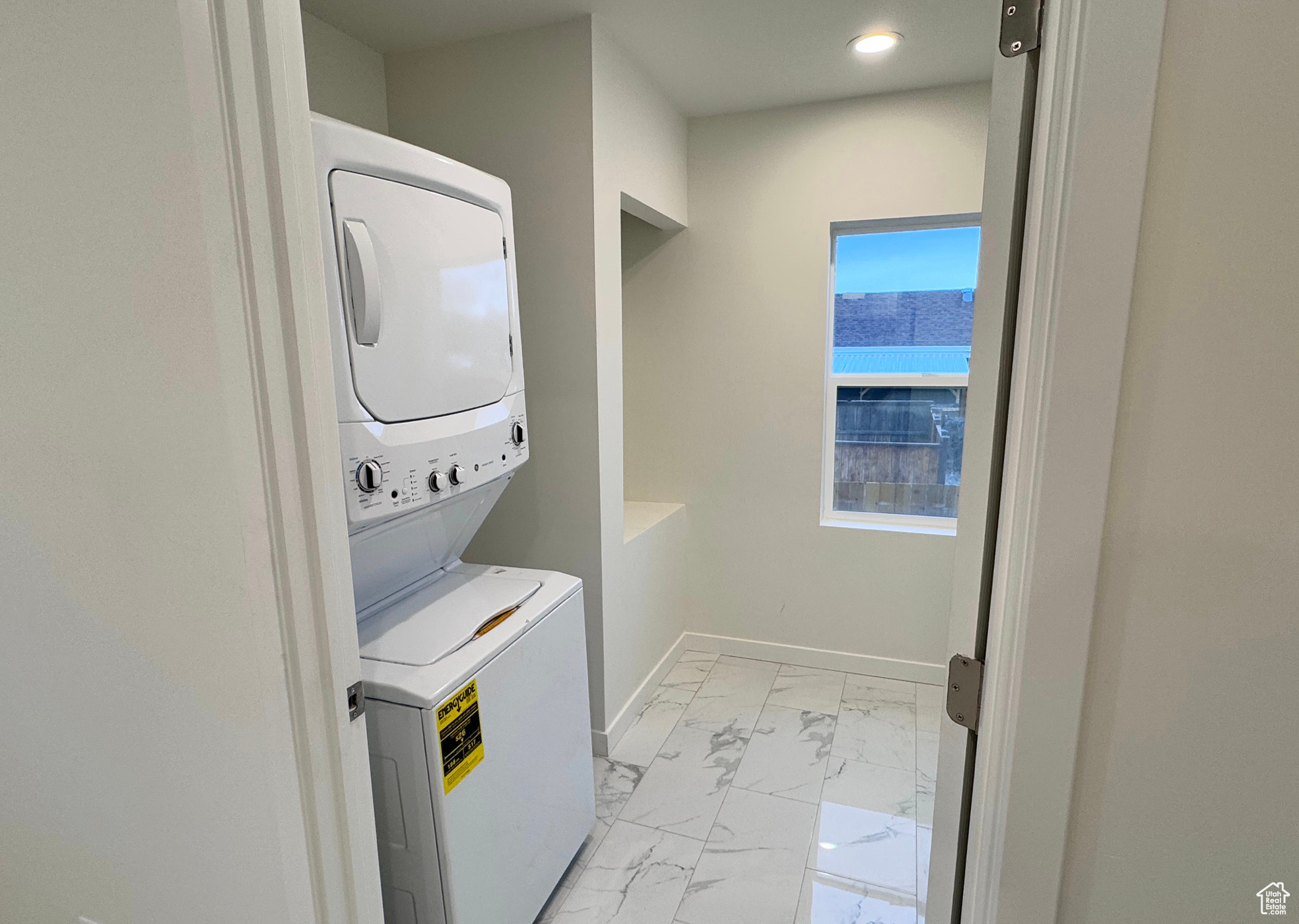 Clothes washing area featuring stacked washing maching and dryer, baseboards, laundry area, and marble finish floor