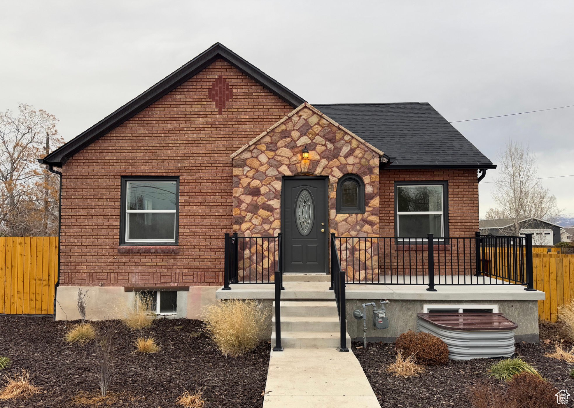 View of front of home featuring stone siding, brick siding, fence, and roof with shingles