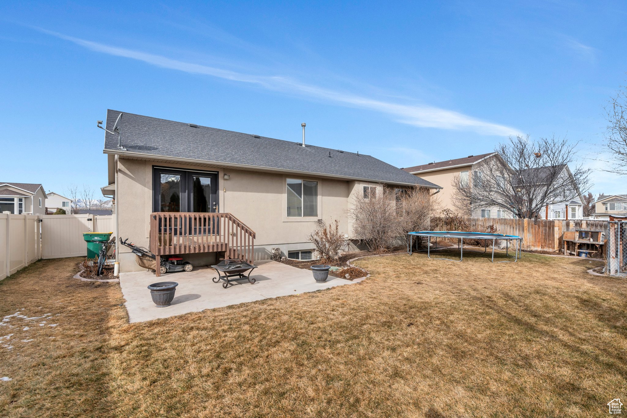 Back of property with a trampoline, a fenced backyard, a patio, and a fire pit
