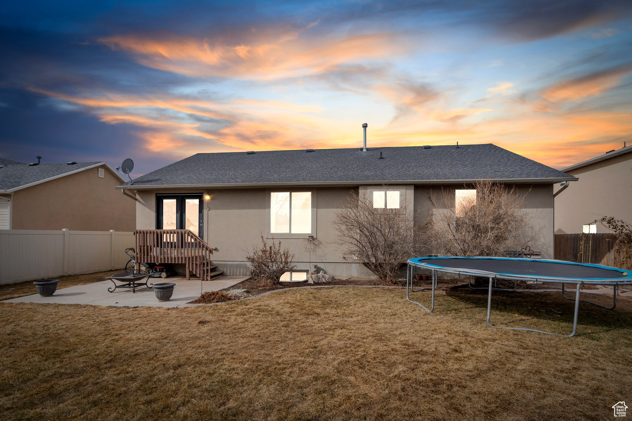 Back of house at dusk featuring a fenced backyard, a trampoline, a lawn, and a patio