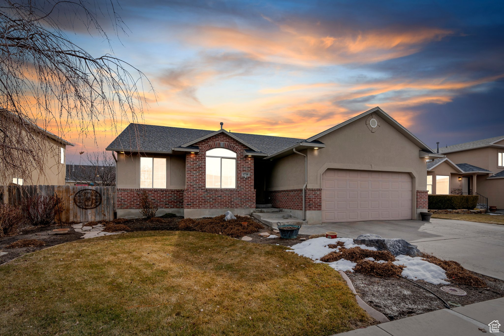 View of front of property featuring a garage, concrete driveway, a lawn, fence, and brick siding