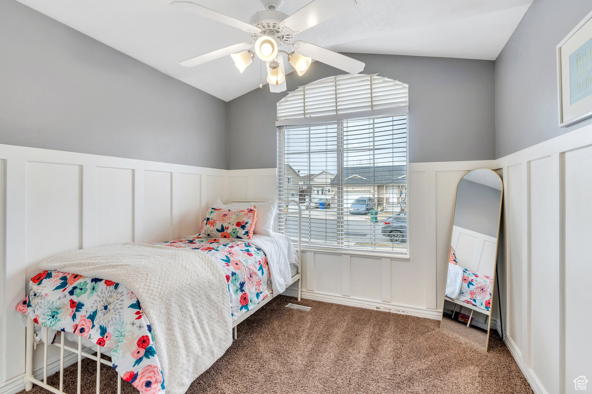 Bedroom featuring a decorative wall, carpet flooring, a ceiling fan, vaulted ceiling, and wainscoting