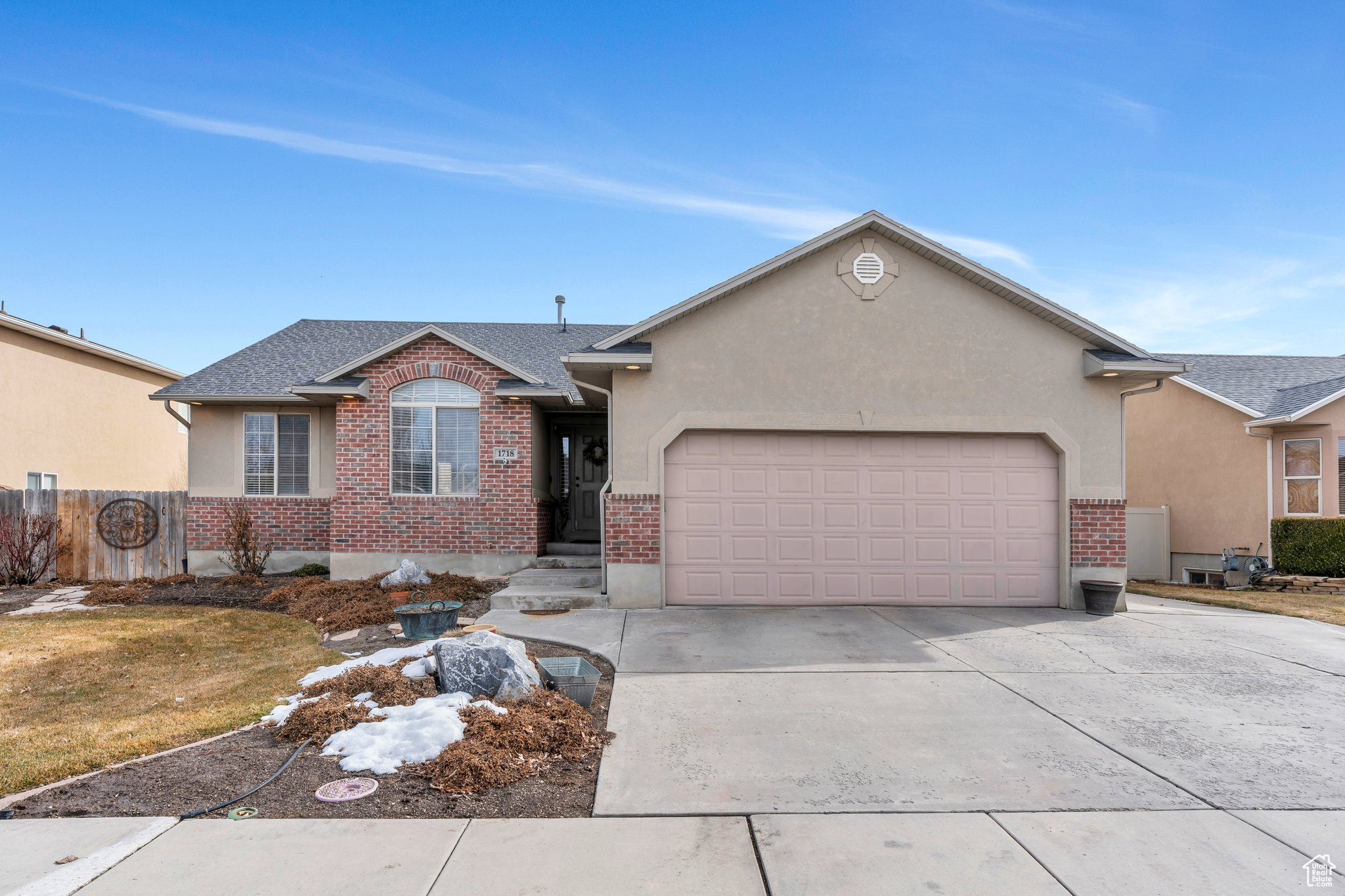 Ranch-style home with driveway, brick siding, an attached garage, fence, and stucco siding