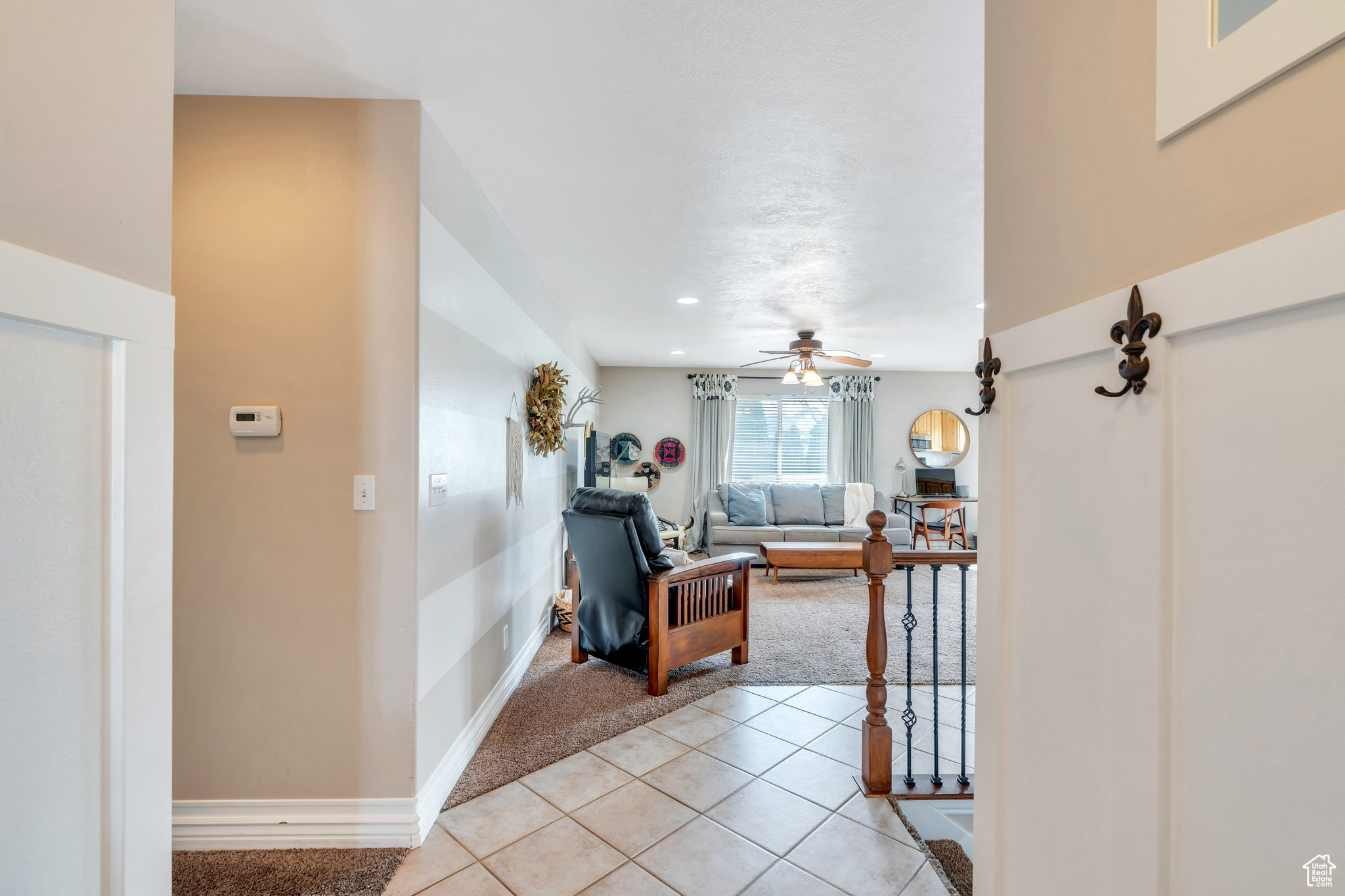 Living area featuring baseboards, light tile patterned flooring, ceiling fan, and light colored carpet