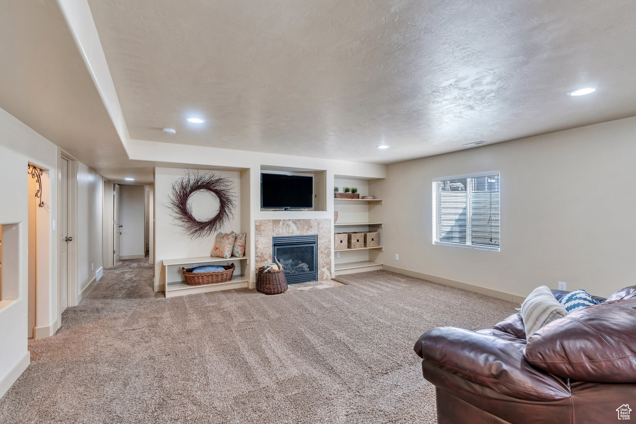 Living room with a textured ceiling, light colored carpet, built in features, baseboards, and a tiled fireplace
