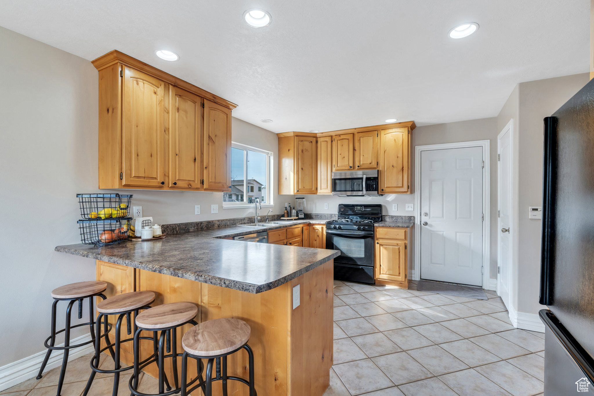 Kitchen with light tile patterned floors, dark countertops, recessed lighting, a peninsula, and black appliances