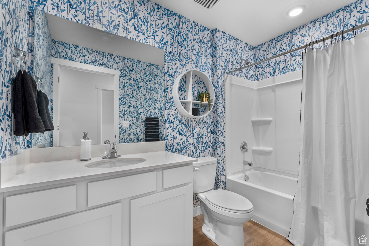 Bathroom with shower / bath combo with shower curtain, wood finished floors, toilet, and wallpapered walls