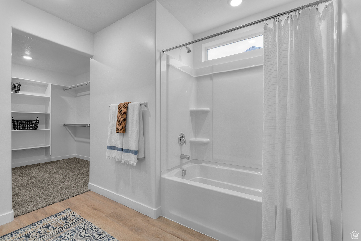 Full bath featuring shower / bath combination with curtain, a spacious closet, baseboards, and wood finished floors