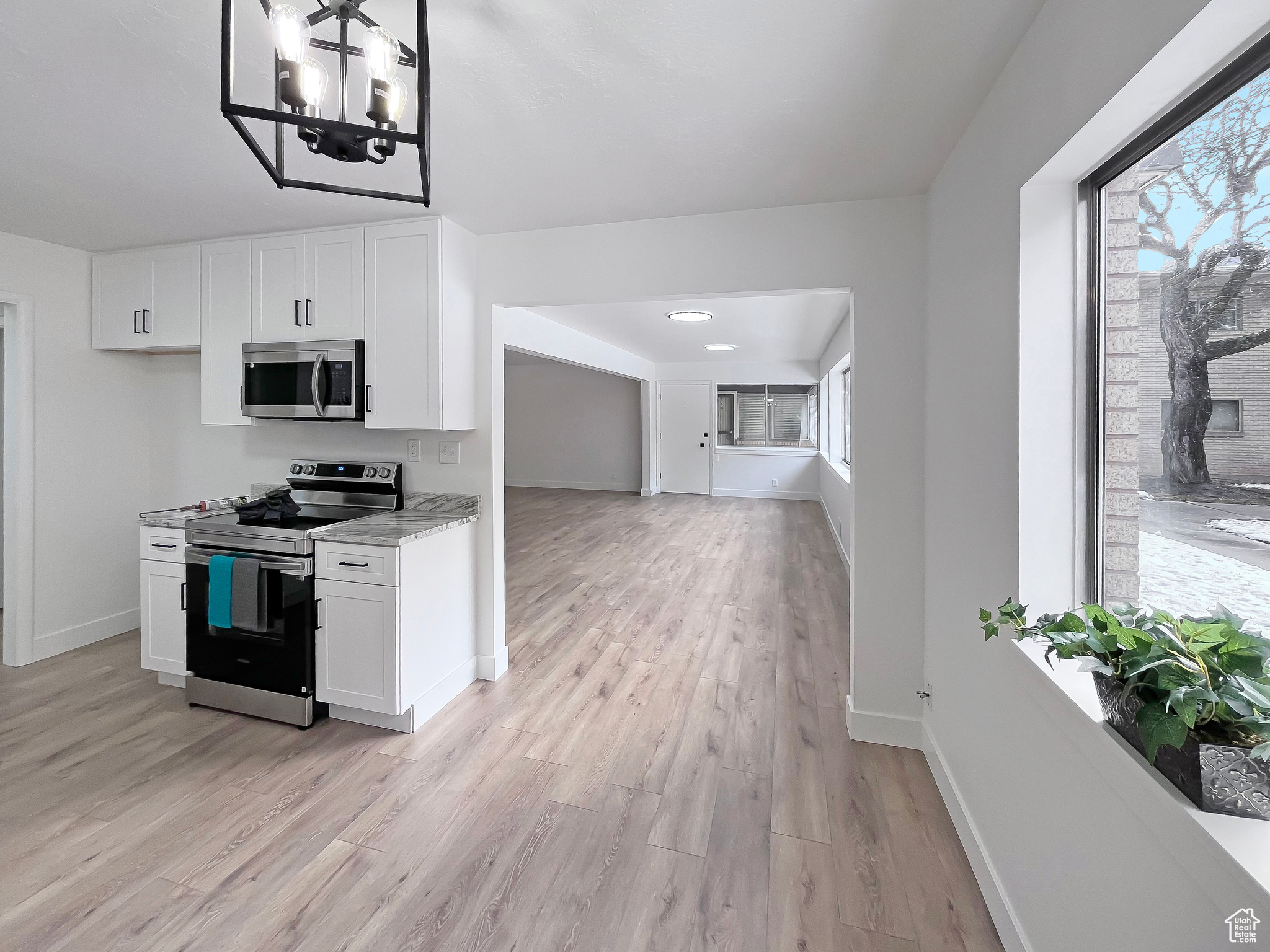 Beautifully updated kitchen with granite countertops, tall white cabinets, light wood-style flooring and stainless-steel appliances, and ample natural light