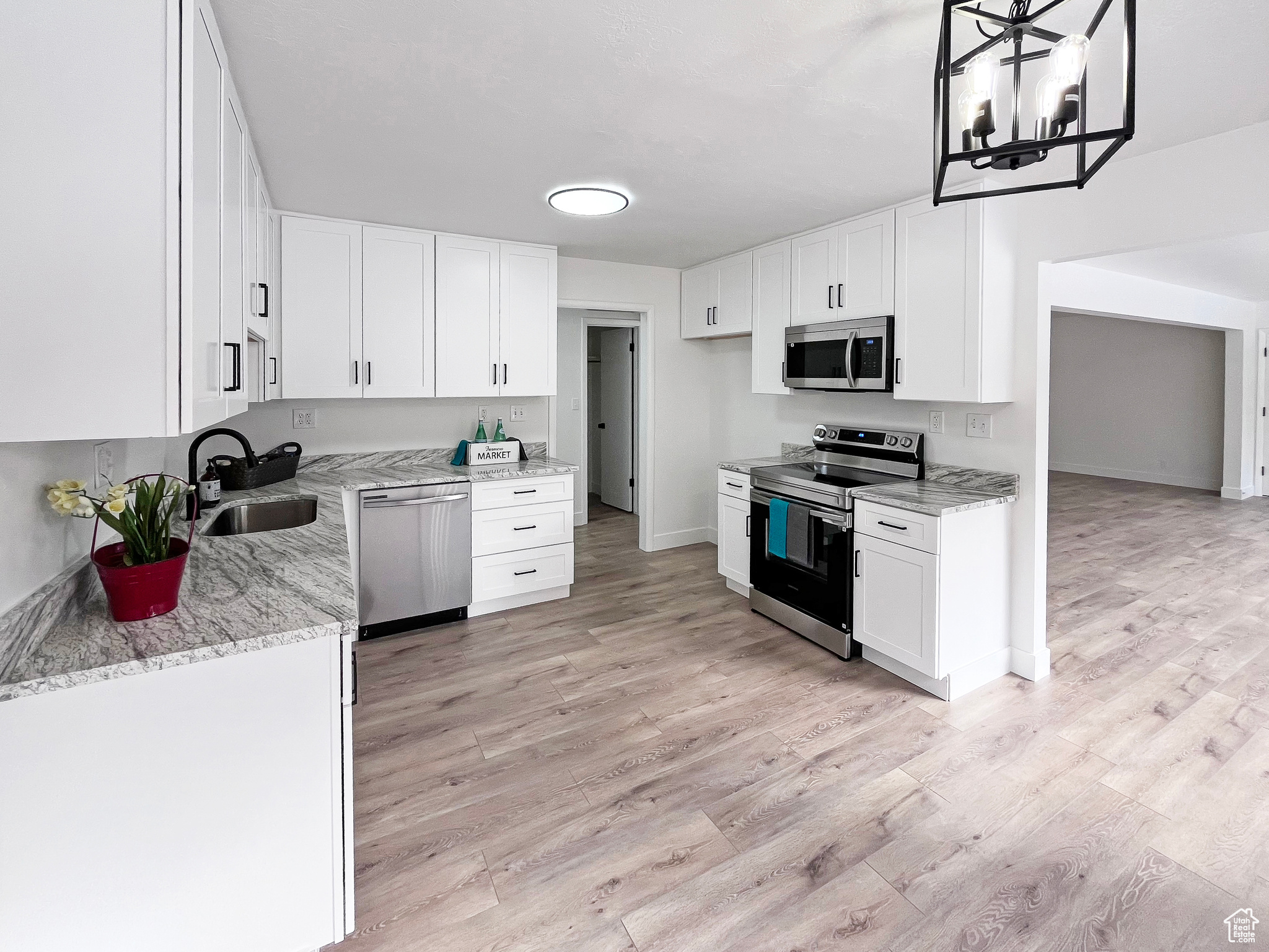 Beautifully updated kitchen with granite countertops, tall white cabinets, light wood-style flooring and stainless-steel appliances, and ample natural light