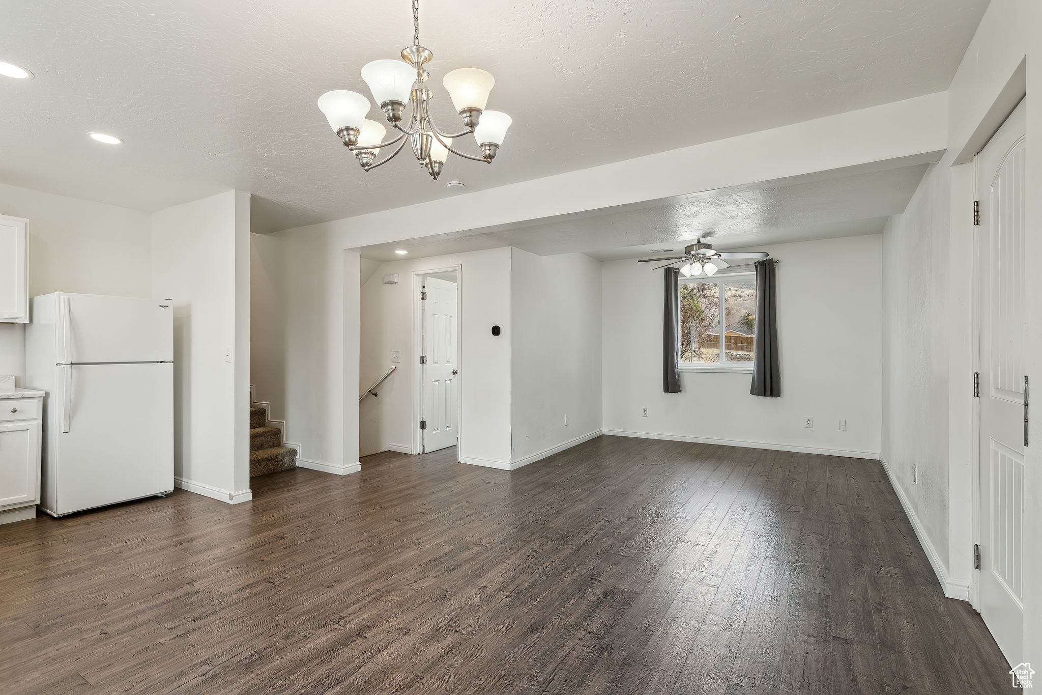 Unfurnished dining area featuring stairs, recessed lighting, dark wood-type flooring, baseboards, and ceiling fan with notable chandelier