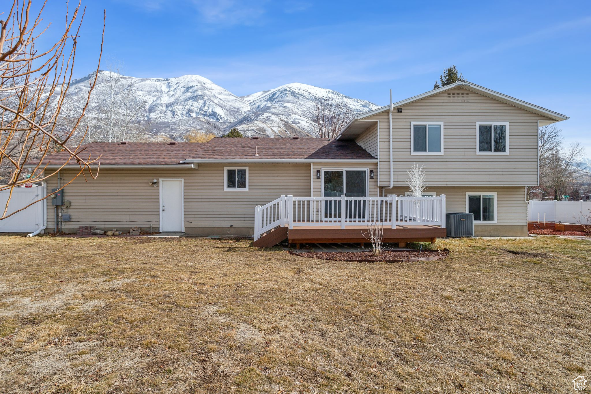 Rear view of house featuring a deck with mountain view, fence, central AC, and a yard