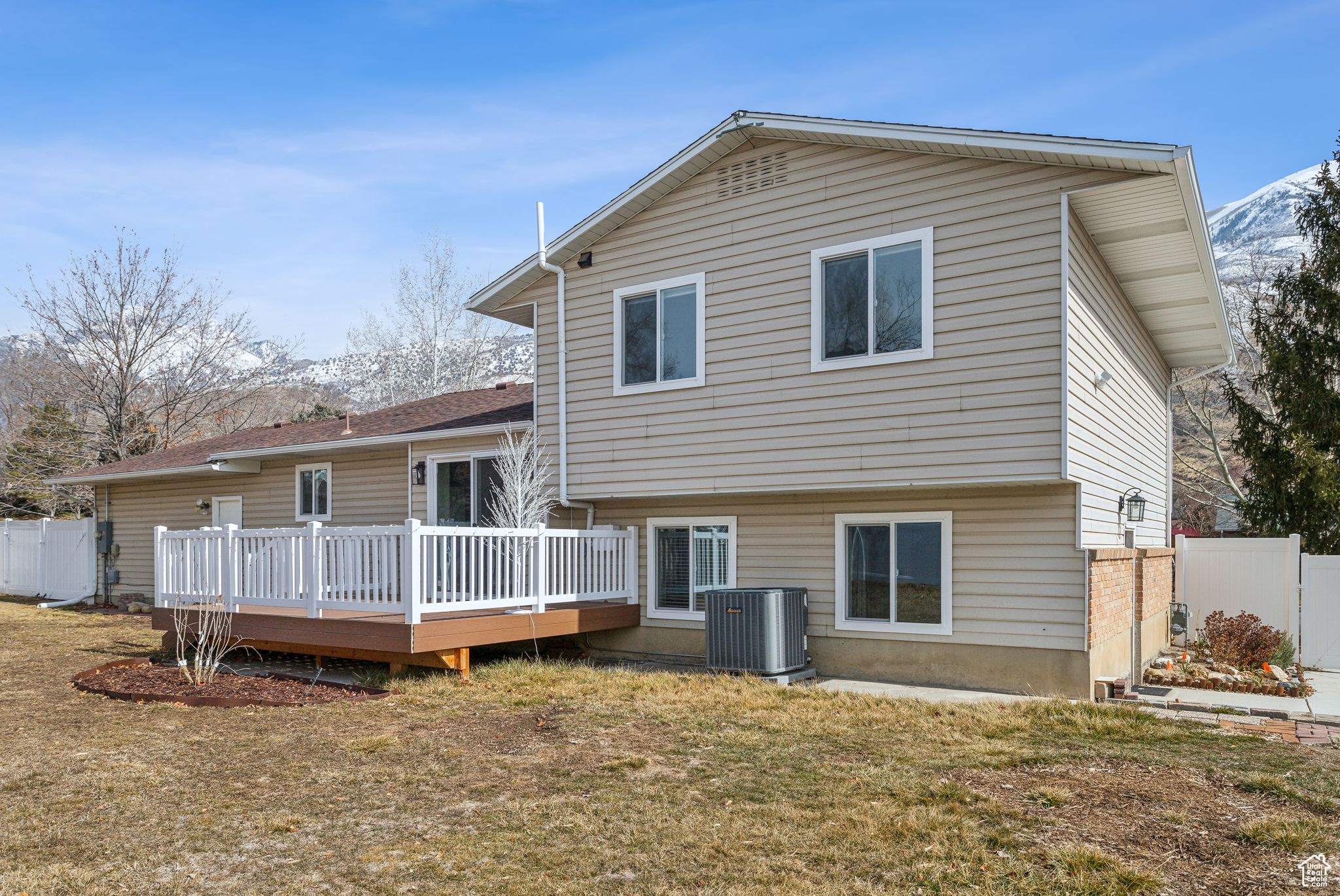 Back of house featuring a deck, a lawn, cooling unit, and fence