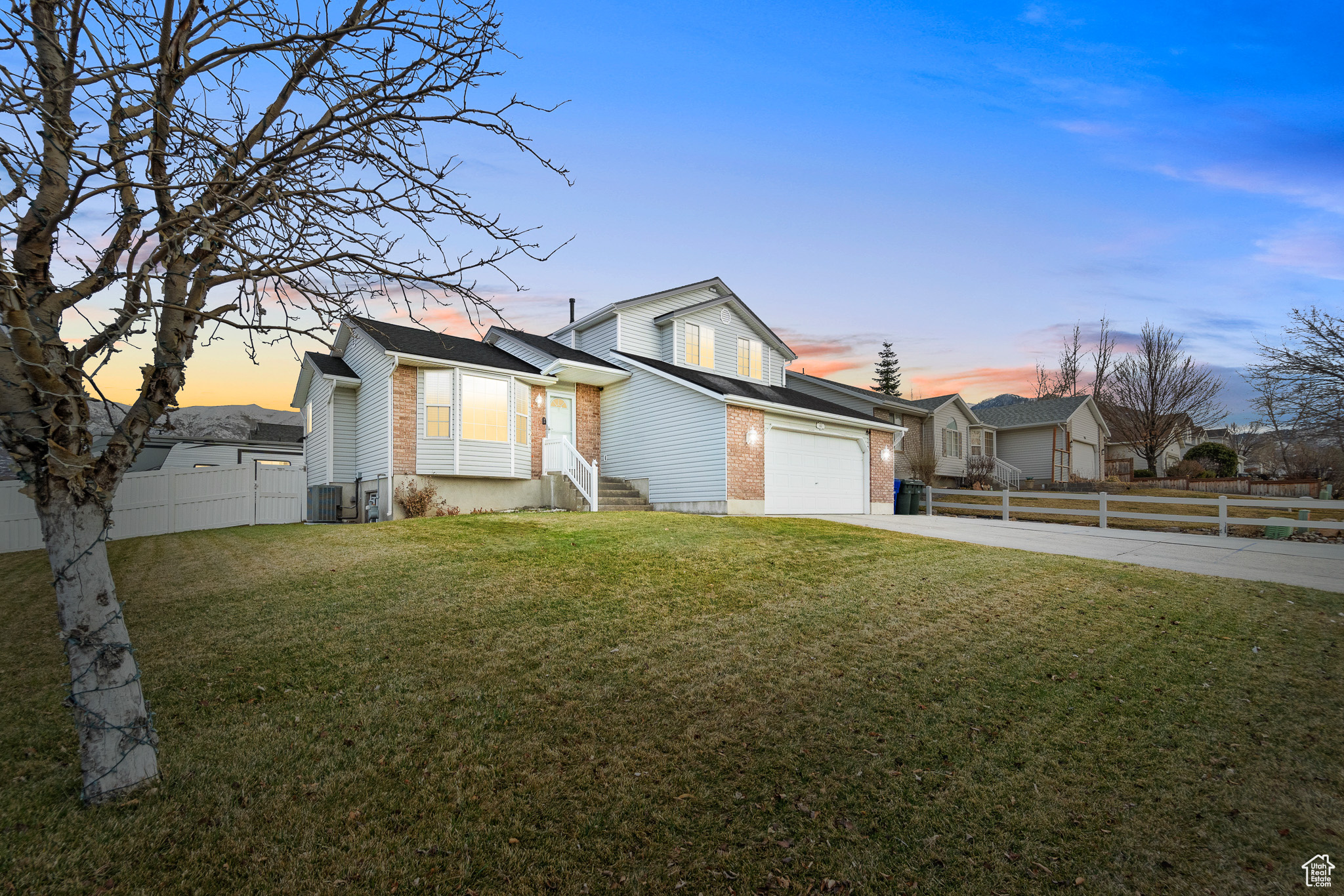 View of front of house with driveway, fence, and a lawn
