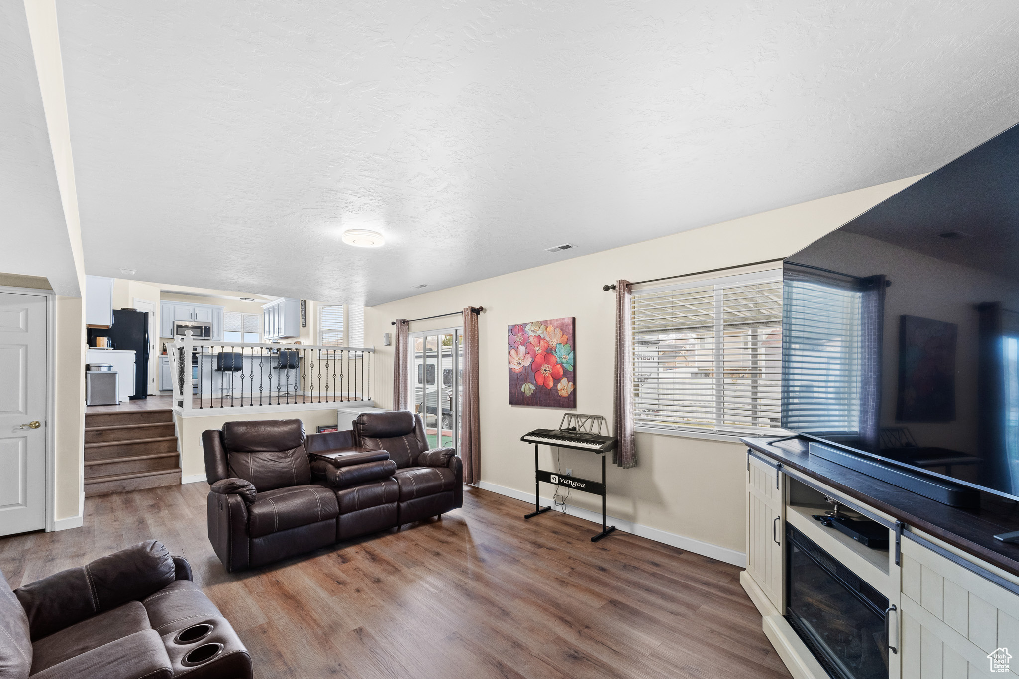 Living area featuring light wood-style flooring, stairs, baseboards, and a textured ceiling