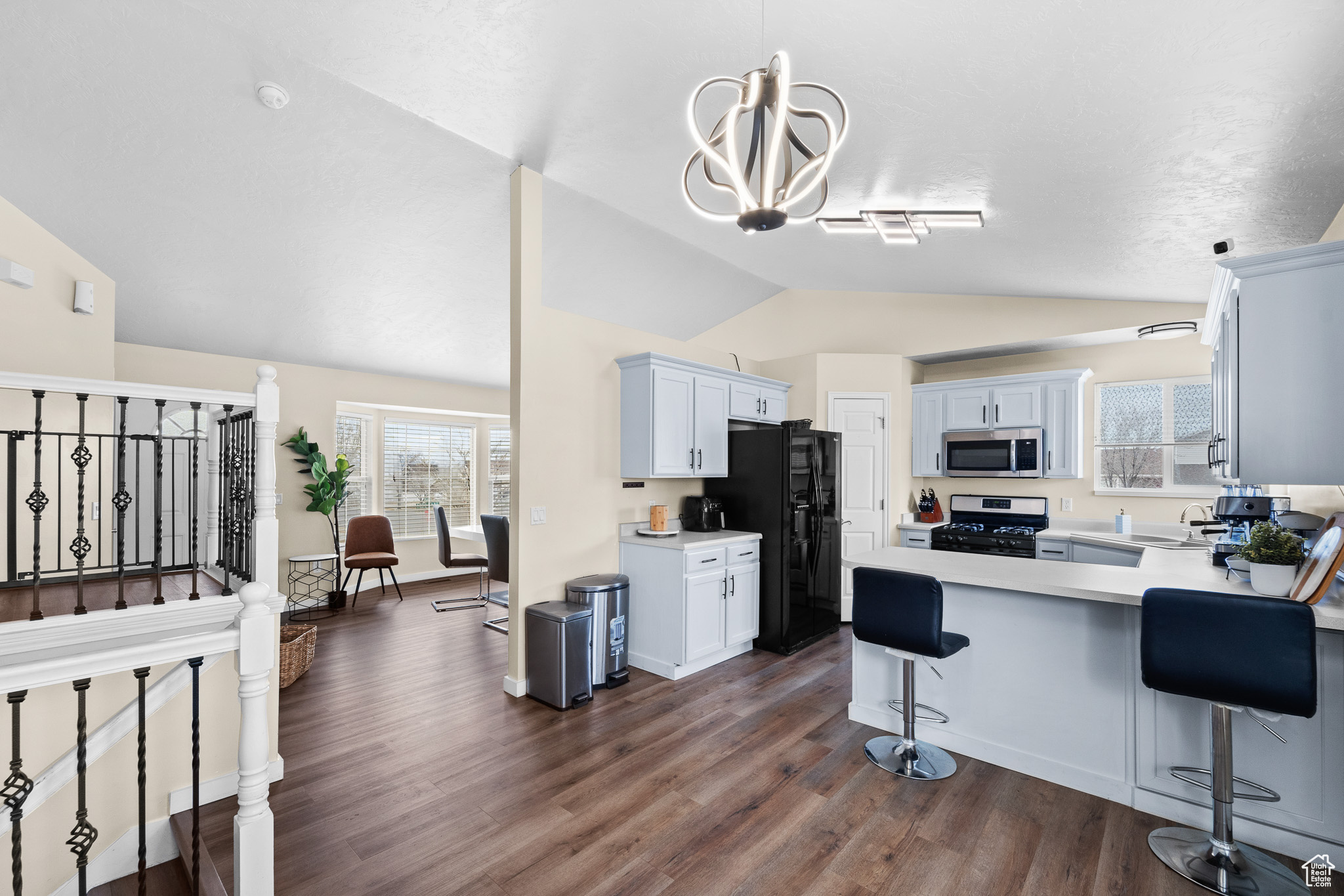 Kitchen featuring stainless steel appliances, white cabinetry, vaulted ceiling, light countertops, and dark wood finished floors
