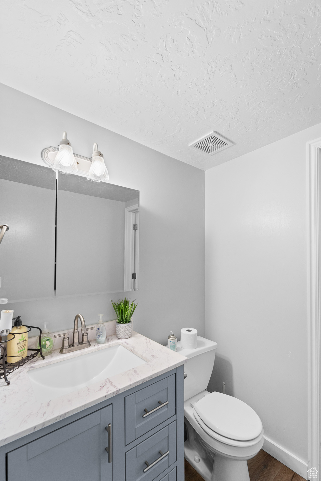 Half bath featuring a textured ceiling, toilet, wood finished floors, vanity, and visible vents