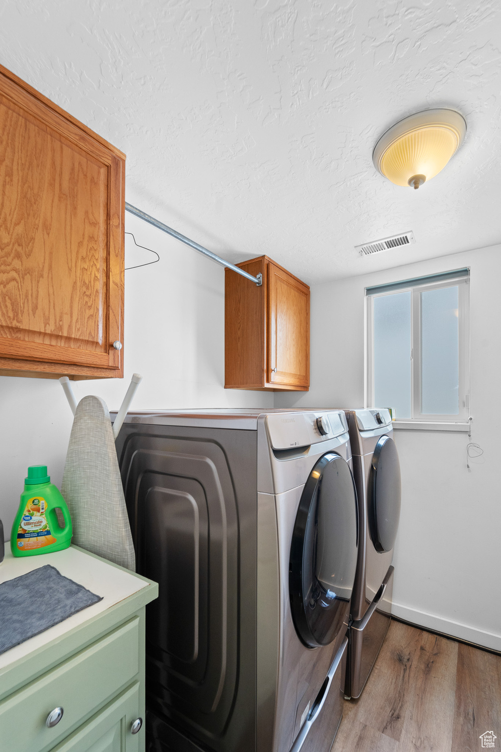 Washroom with dark wood-style flooring, cabinet space, visible vents, a textured ceiling, and separate washer and dryer
