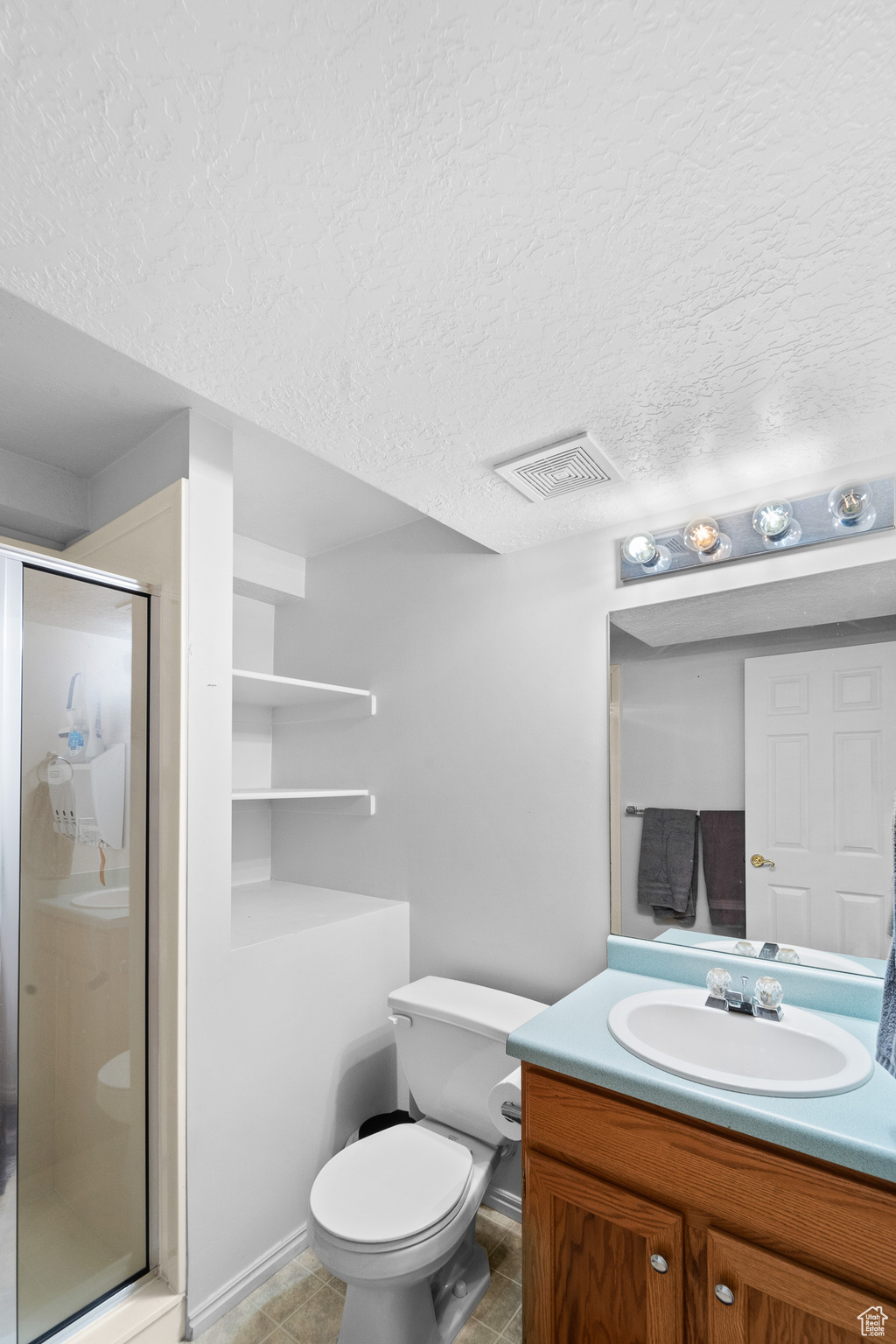 Full bathroom with a textured ceiling, vanity, a shower stall, and visible vents