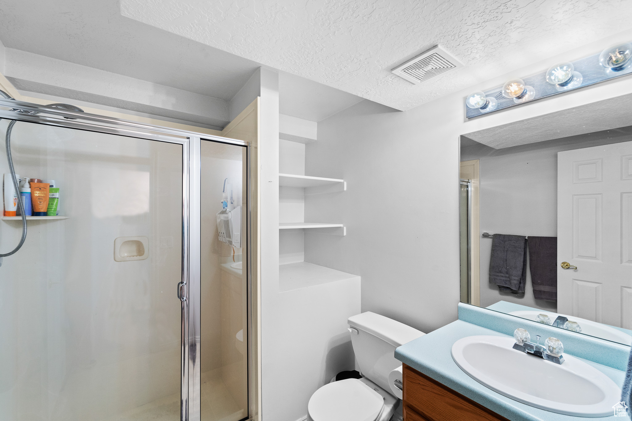 Bathroom with a stall shower, visible vents, vanity, and a textured ceiling