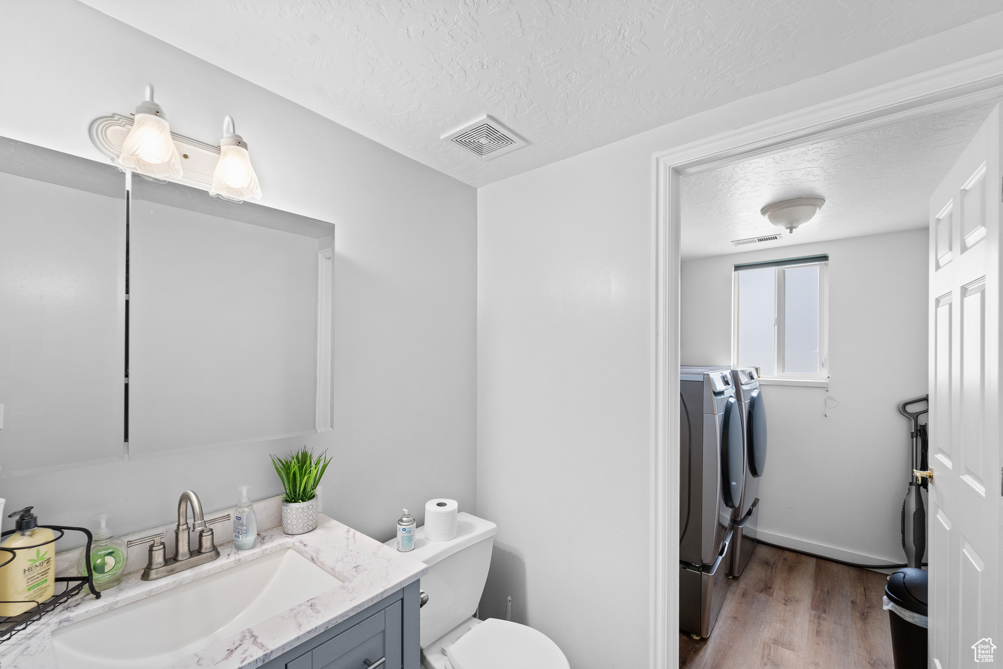 Bathroom with washing machine and clothes dryer, visible vents, vanity, a textured ceiling, and wood finished floors