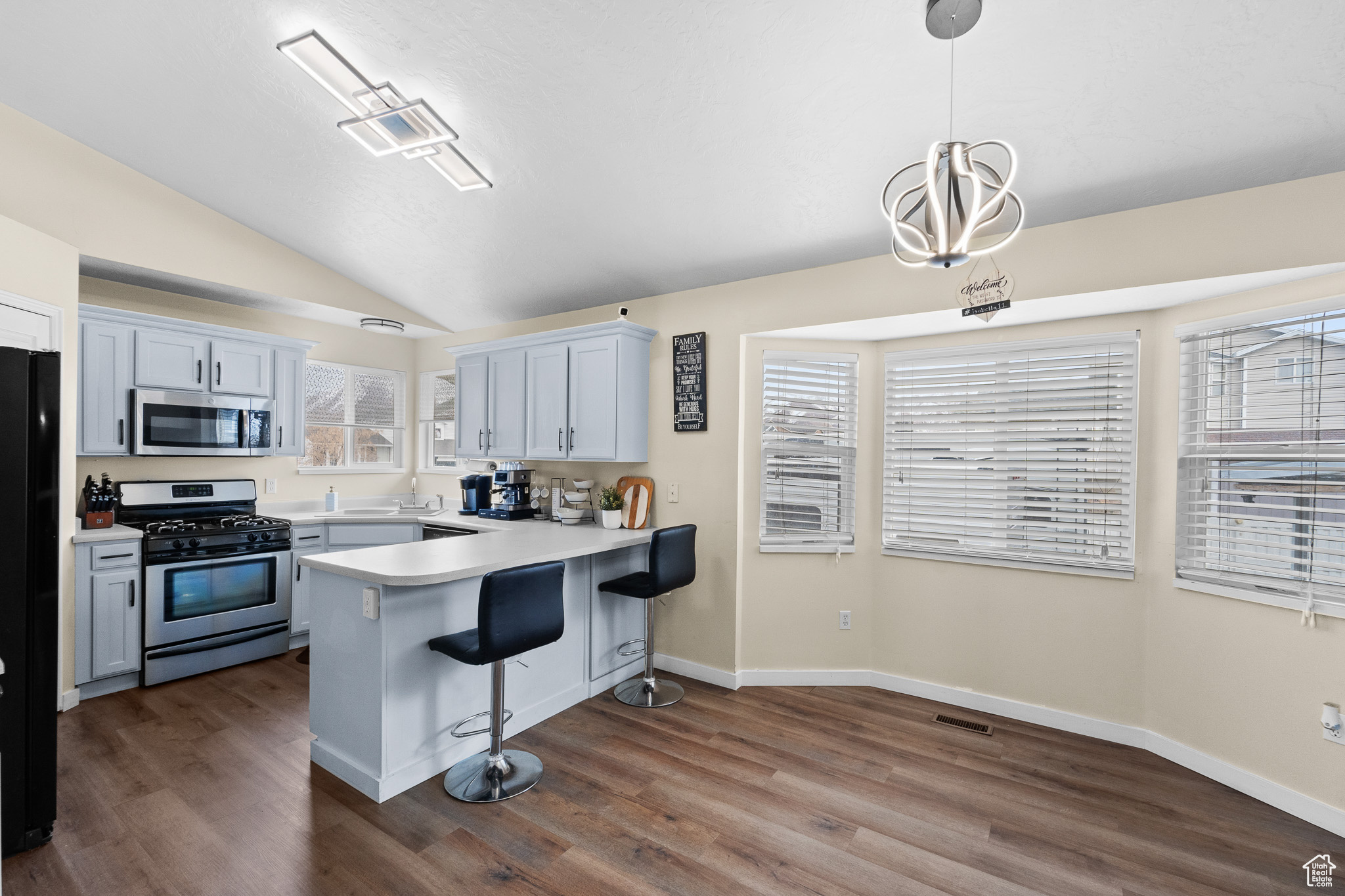 Kitchen with appliances with stainless steel finishes, a breakfast bar, a peninsula, hanging light fixtures, and light countertops