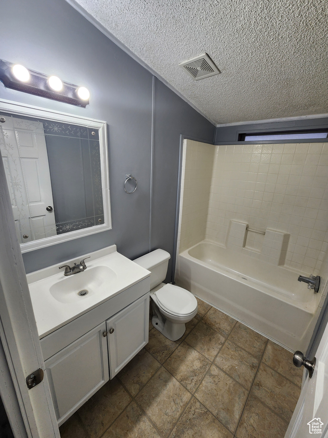 Full bathroom with a textured ceiling, toilet, vanity, visible vents, and shower / bathing tub combination