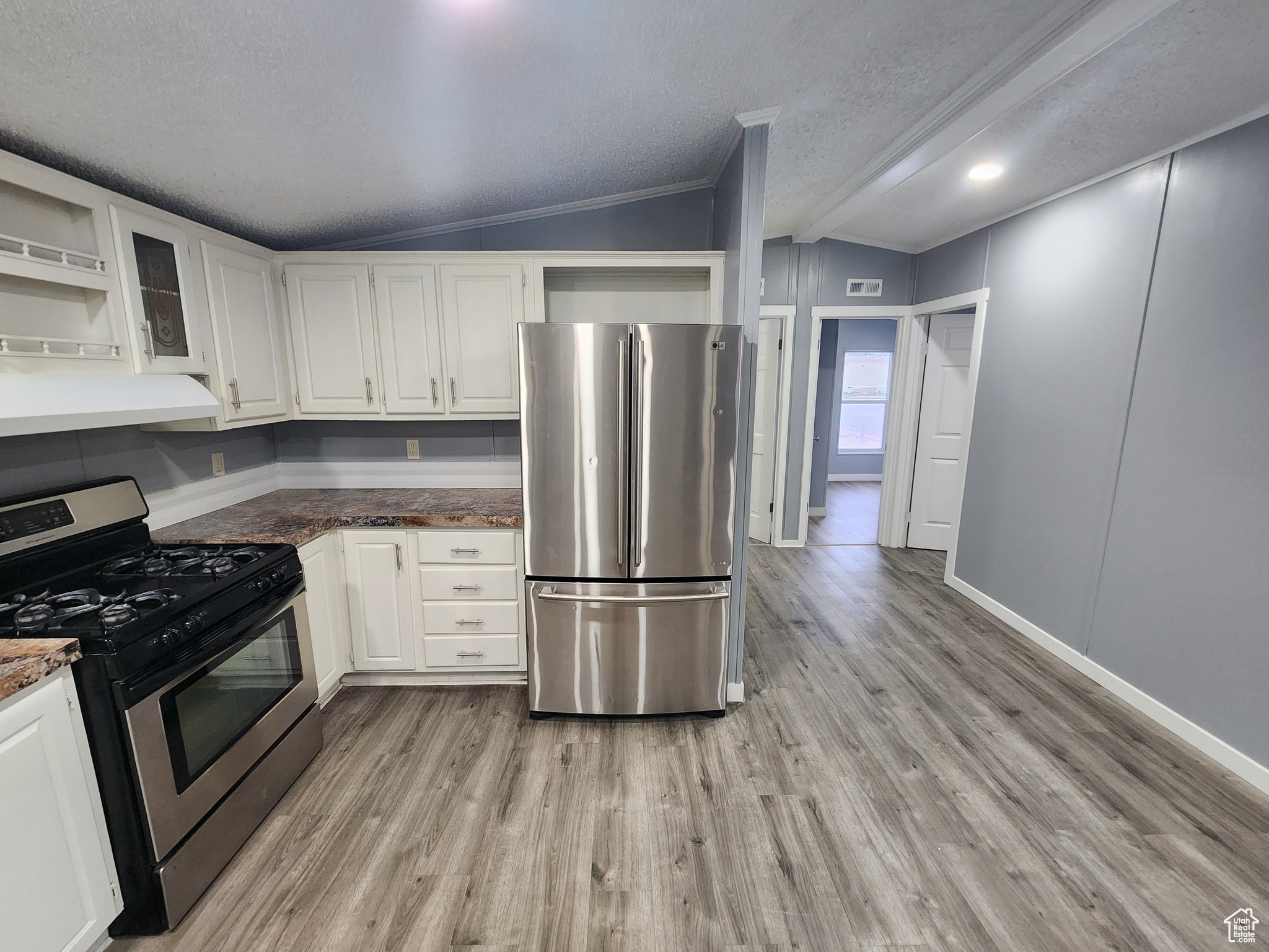 Kitchen featuring appliances with stainless steel finishes, glass insert cabinets, dark countertops, and white cabinetry