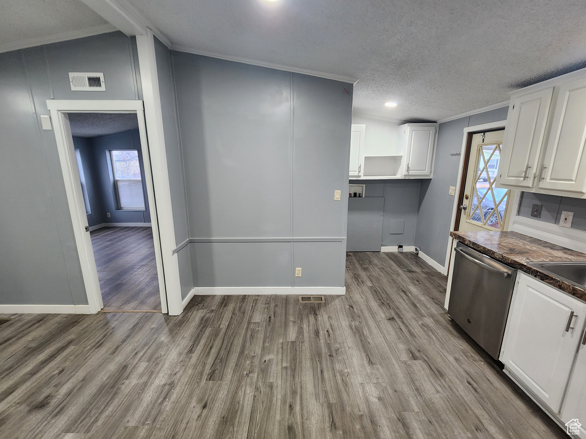 Kitchen featuring light wood-type flooring, dark countertops, white cabinetry, and dishwasher