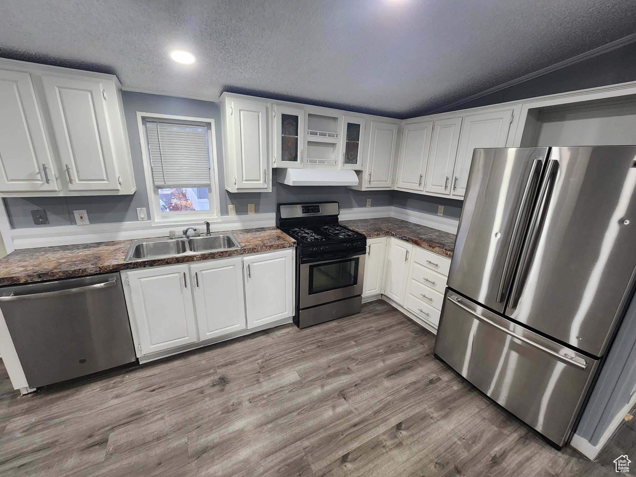 Kitchen featuring white cabinets, dark countertops, glass insert cabinets, appliances with stainless steel finishes, and a sink