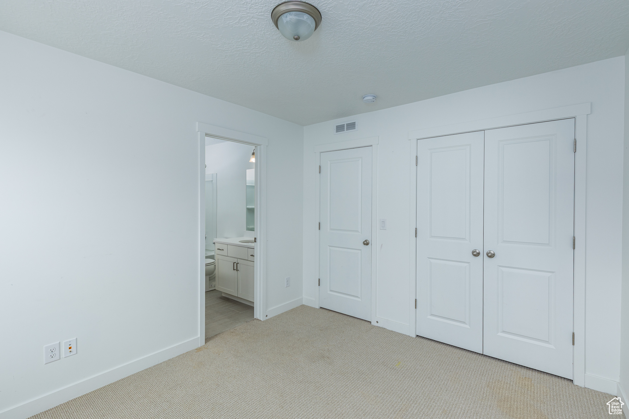 Unfurnished bedroom with a closet, visible vents, light carpet, a textured ceiling, and baseboards